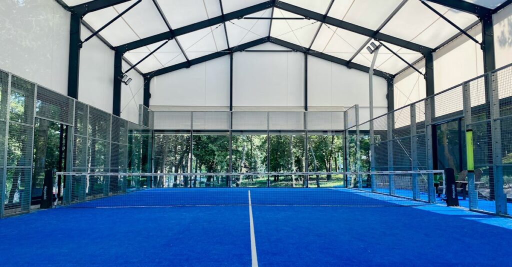 Spacious indoor padel court with vibrant blue flooring under a wide roof.